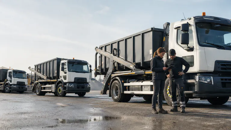 Responsable d’exploitation et conducteur devant une flotte de camions ampliroll.
